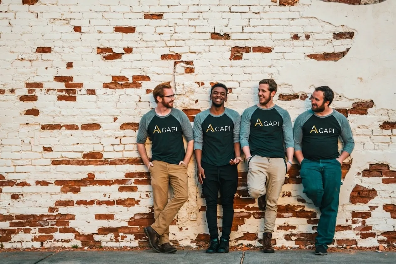 The Agapi team in branded shirts, leaning against a brick wall
